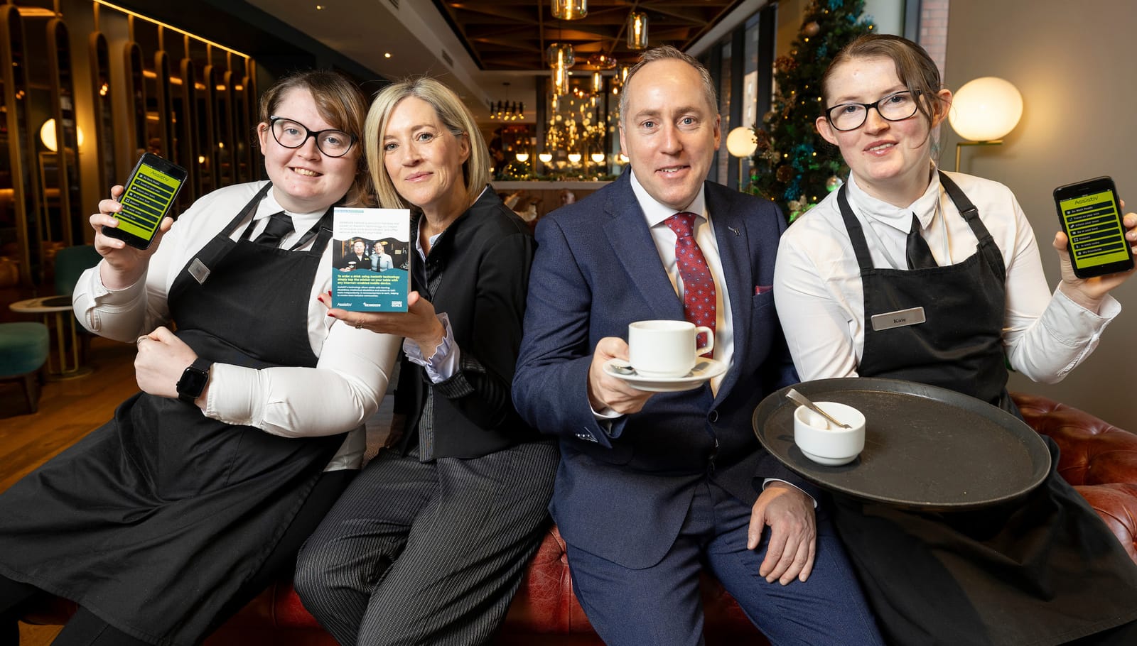 Emma and Kate, holding their phones with AssistiV, with Declan Curtis and a colleague at the Hyatt Centric
